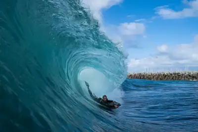 Bodyboarder riding inside a turquoise wave beneath a blue sky