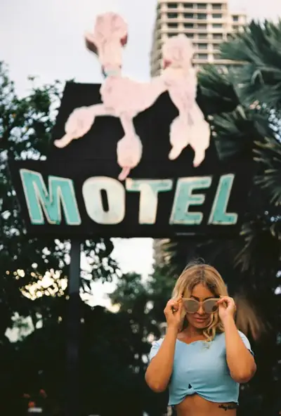 Woman adjusting round sunglasses beneath a vintage motel sign