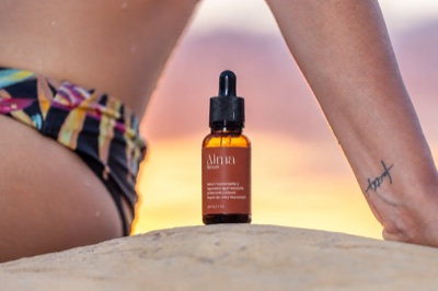 Amber glass dropper bottle on sand between a seated person’s legs