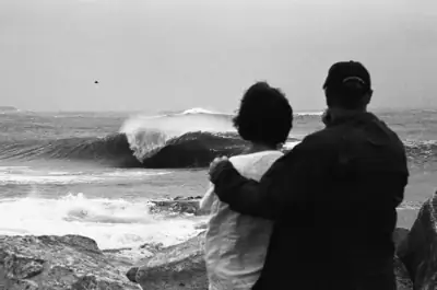 Couple standing together above a surf break, in black and white