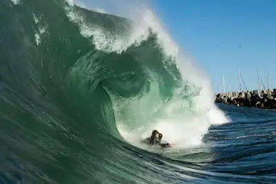 Bodyboarder riding a steep green wave beside a rocky breakwater