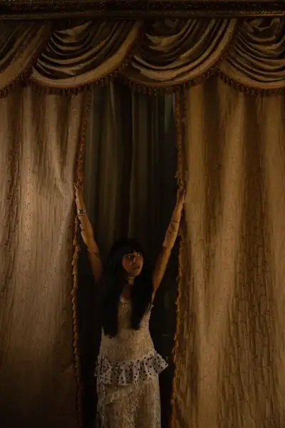 Woman raising her arms between heavy curtains beneath an ornate pelmet