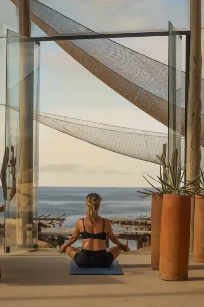 Woman sitting cross-legged on a coastal terrace beneath a shade sail