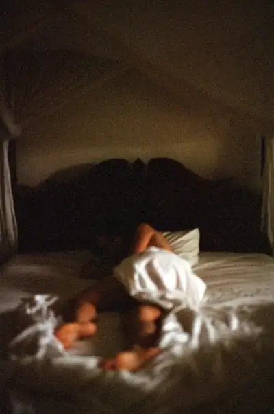 Woman reclining on a bed in warm light inside a dark room