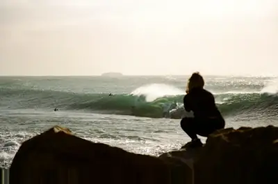 Person sitting on rocks watching rolling ocean waves