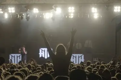 Concert audience beneath bright stage lights with an arm raised in the foreground