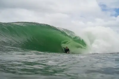 Bodyboarder riding deep inside a large emerald-green wave