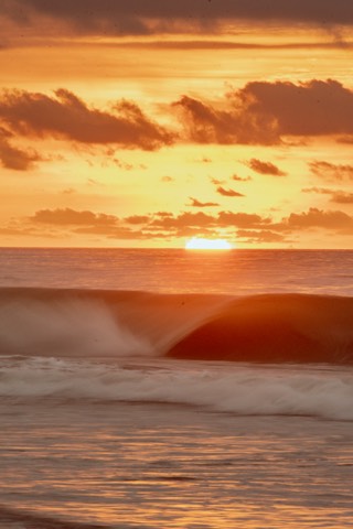Orange sunset above a breaking ocean wave and sea spray
