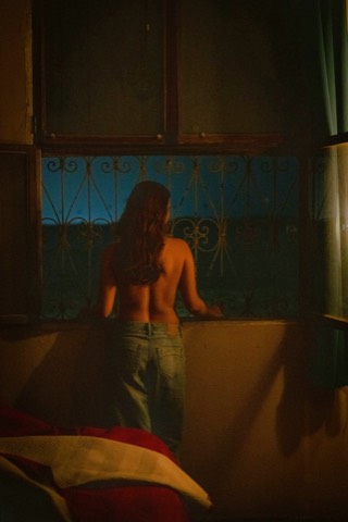 Woman seated beside a window in a dim room with warm light